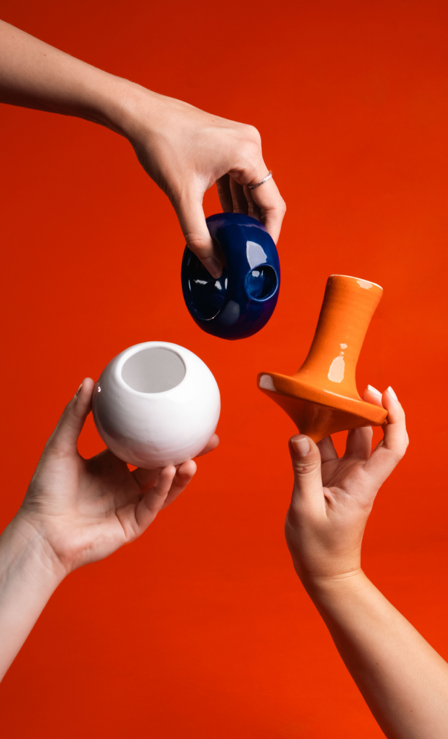 Three hands holding blue, white, and orange ceramic game objects