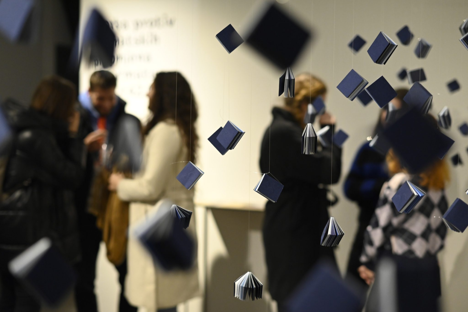 Visitors viewing suspended miniature blue books at the Plastic Waste in the Sea exhibition