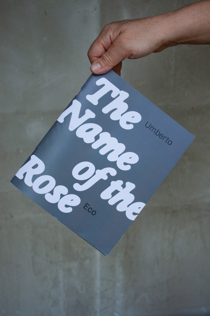 A hand holding the blue cover of The Name of the Rose experimental book